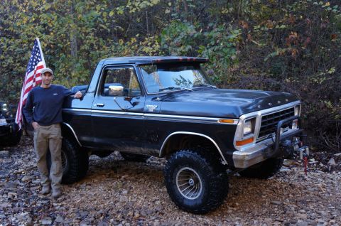 1979 Ford Bronco - A man poses with a lifted Ford Bronco, an American flag flying nearby, and another vehicle in the background.