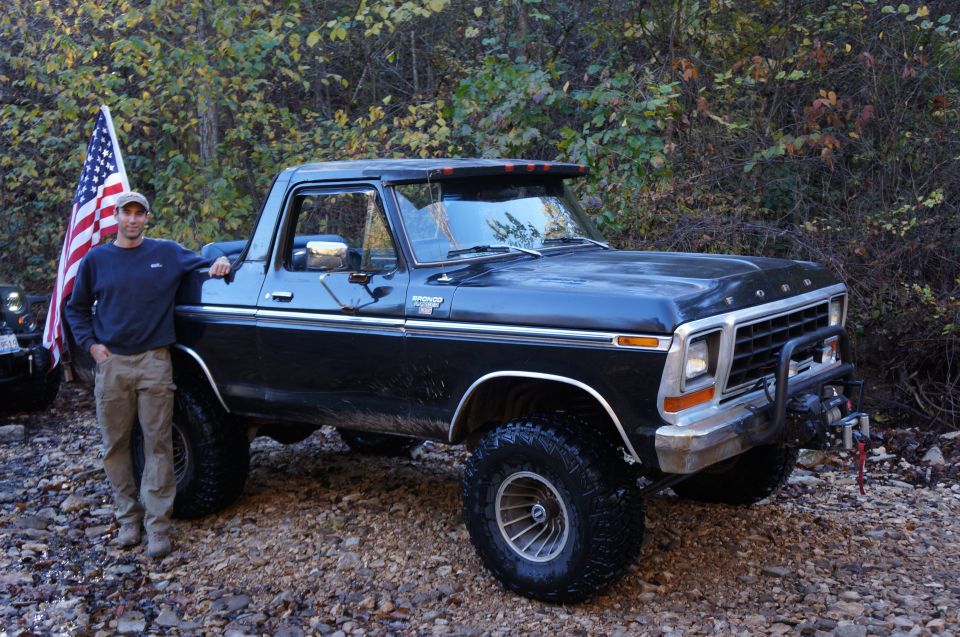 Man standing by lifted black Ford Bronco with American flag. Another vehicle partially visible