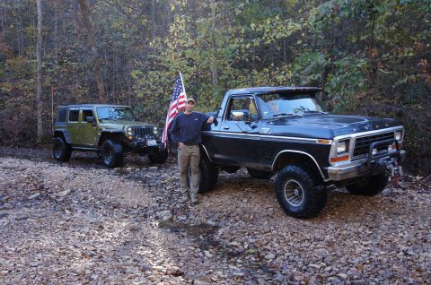 1979 Ford Bronco - A man stands next to a black 1979 Ford F-150 pickup truck, with a green Jeep in the background.