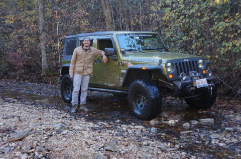 1979 Ford Bronco - A man poses with a lifted green Jeep Wrangler off-road, navigating a rocky stream bed.