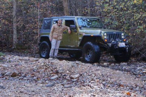 1979 Ford Bronco - A man poses with his modified Jeep Wrangler on a wooded trail during autumn.
