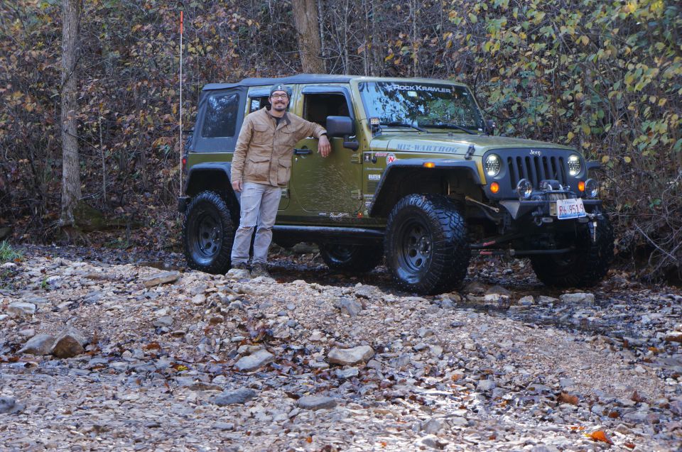 Man standing next to a green Jeep Wrangler on a rocky trail