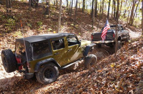 1979 Ford Bronco - Two off-road vehicles navigate a wooded trail covered in fallen autumn leaves.