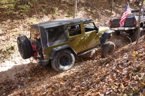 1979 Ford Bronco - Two off-road vehicles navigate a wooded trail covered in autumn leaves.