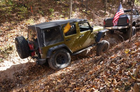 1979 Ford Bronco - Two off-road vehicles navigate a wooded trail covered in fallen autumn leaves.