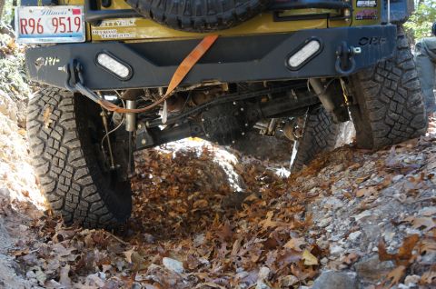 1979 Ford Bronco - The rear of a yellow off-road vehicle navigates a leaf-covered dirt trail.