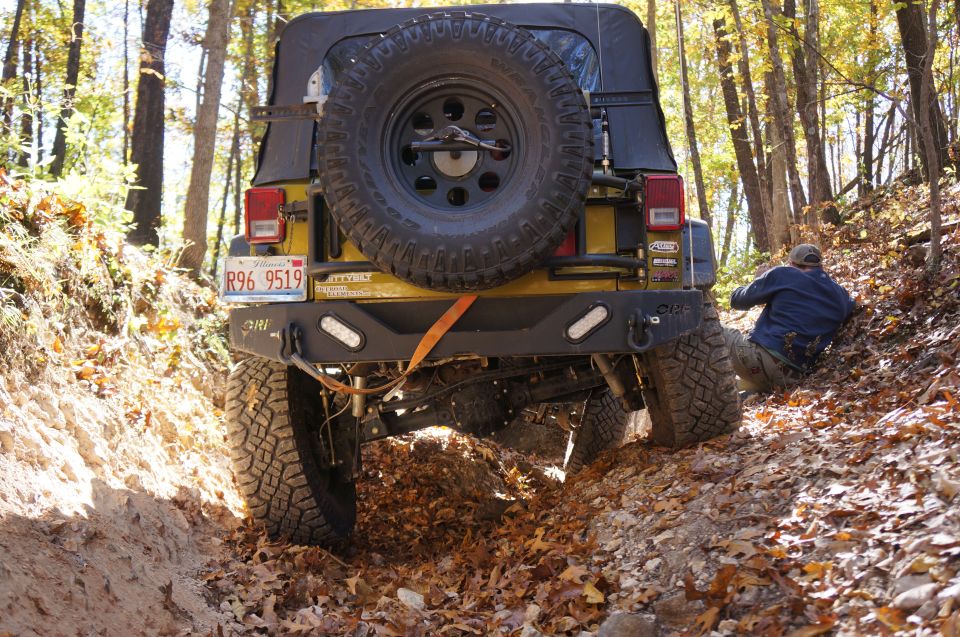 Yellow Jeep Wrangler rear view on a dirt trail with a person in the background