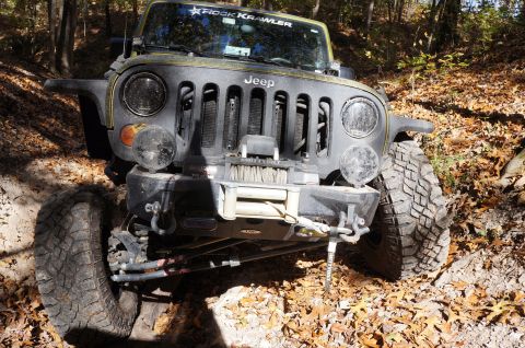1979 Ford Bronco - Jeep Wrangler navigates an off-road trail covered in autumn leaves. The vehicle has a winch and "Rock Krawler" decal.