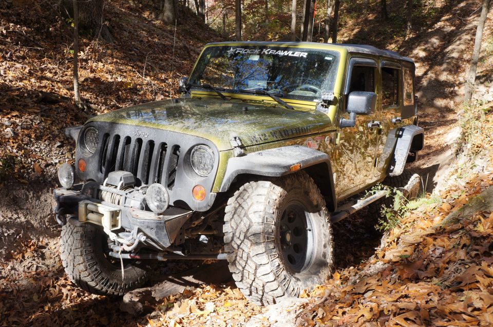 Yellow Jeep Wrangler with "Rock Krawller" sticker on windshield, off-roading on a dirt trail