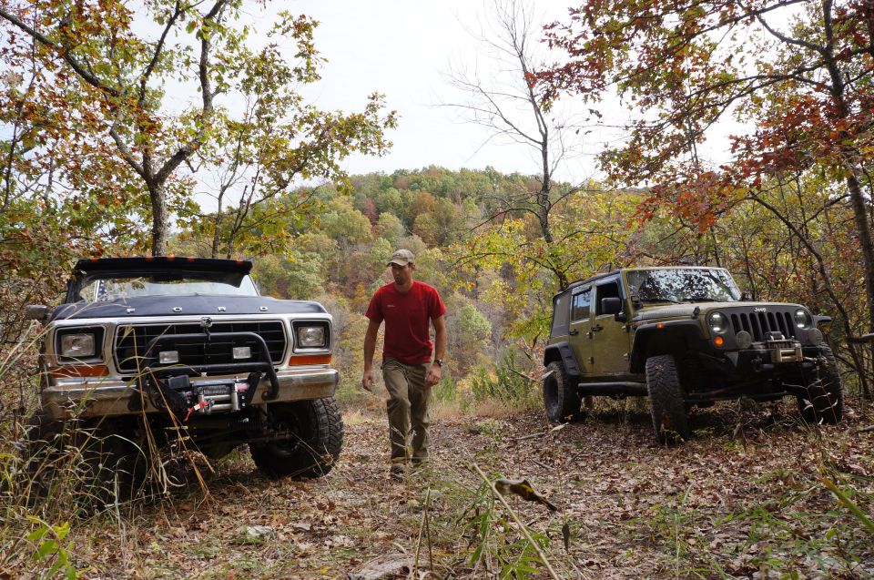 Ford Bronco and Jeep Wrangler parked on a dirt path in autumn woods. Man walks between them