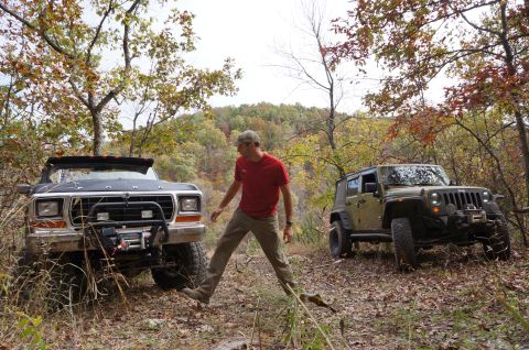 1979 Ford Bronco - Two off-road vehicles are parked on a dirt path surrounded by trees with autumn foliage.