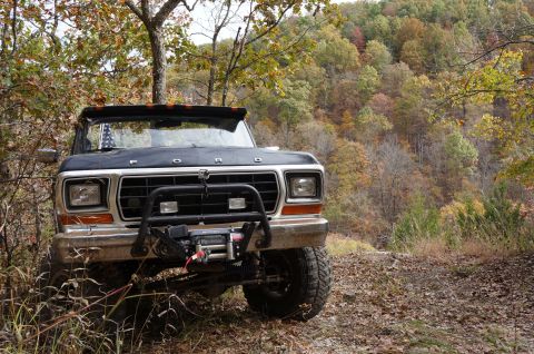 1979 Ford Bronco - A Ford Bronco is parked on a wooded trail during autumn, with colorful leaves on the trees.