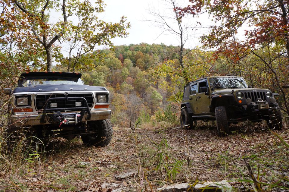 Dark blue Ford Bronco with a winch and a green Jeep Wrangler on a wooded trail