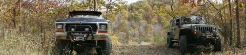 1979 Ford Bronco - Two off-road vehicles, a 1979 Ford Bronco and a Jeep Wrangler, are parked on a dirt path during autumn.