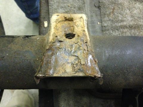 1979 Ford Bronco - A heavily rusted metal bracket is attached to a dark, cylindrical vehicle frame component.