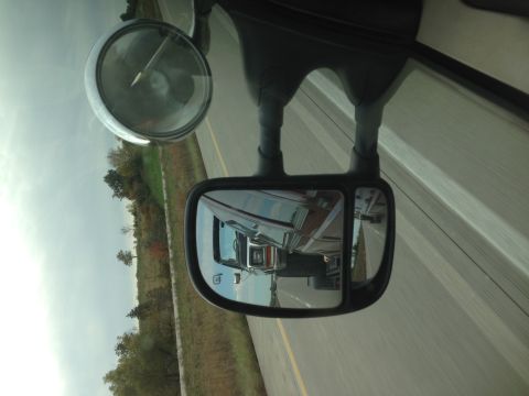 1979 Ford Bronco - The reflection in the truck's side mirror shows a trailer being towed on the highway.