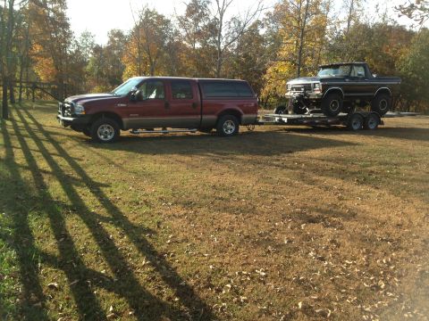 1979 Ford Bronco - A dark 1979 Ford Bronco is transported on a trailer towed by a red Ford F-250 pickup truck.