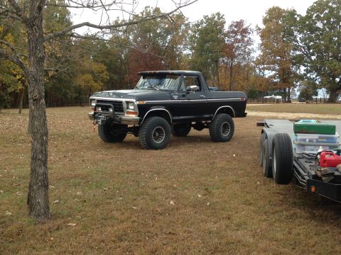 1979 Ford Bronco - Lifted black Ford Bronco with off-road tires and winch, parked outdoors next to a trailer.