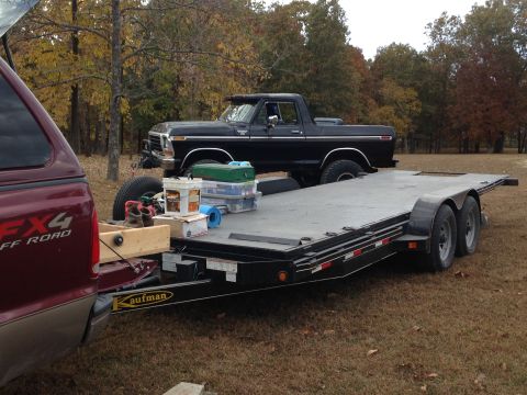 1979 Ford Bronco - A black Ford Bronco is loaded onto a trailer, hitched to a red pickup truck, with autumn trees in the background.
