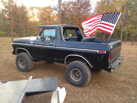 1979 Ford Bronco - Black Ford Bronco with an American flag flying from the tailgate, parked on dry grass.