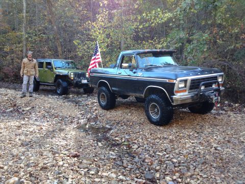 1979 Ford Bronco - A man stands next to a green Jeep while a black 1979 Ford Bronco is parked in front on a wooded trail.