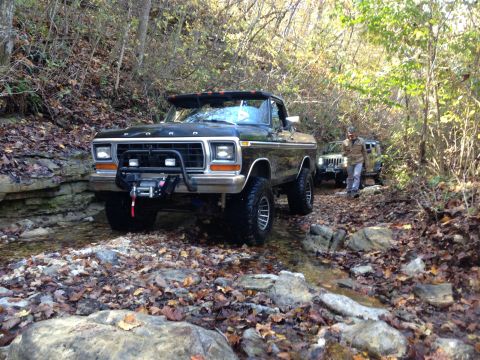 1979 Ford Bronco - A lifted black 1979 Ford Bronco navigates a rocky stream during an off-road excursion, with another vehicle following behind.