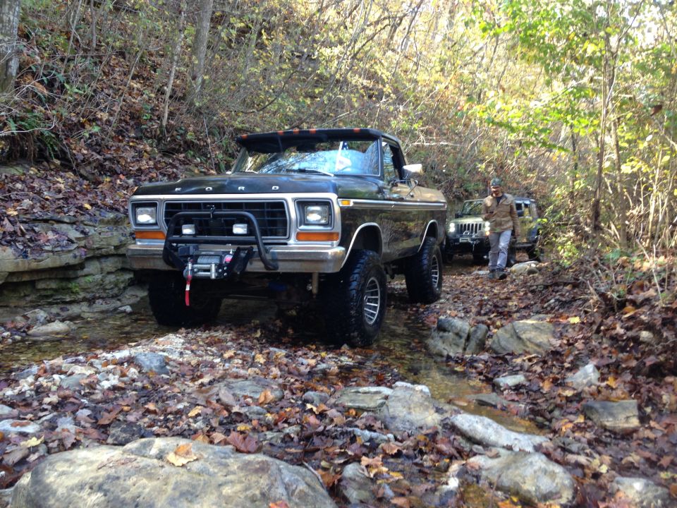 Black 1979 Ford Bronco with winch driving through a rocky stream bed