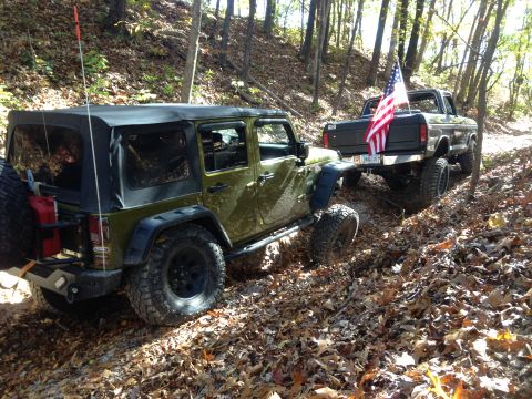 1979 Ford Bronco - Two off-road vehicles, a Jeep and a pickup truck, navigate a wooded trail in the fall.