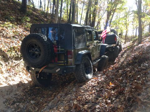 1979 Ford Bronco - Two off-road vehicles navigate a leaf-covered path through a forest during autumn.