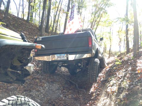 1979 Ford Bronco - A black 1979 Ford Bronco flies an American flag while navigating an off-road trail.