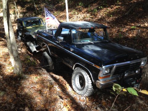 1979 Ford Bronco - A black 1978 Ford Bronco is seen off-roading on a wooded trail, followed by a green Jeep.