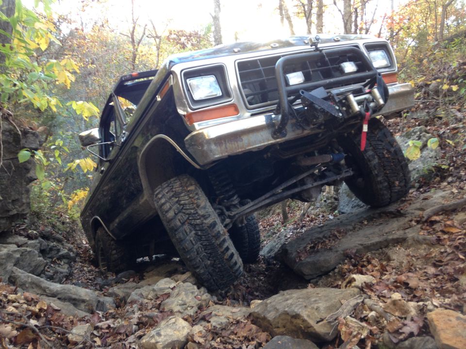 Black Ford Bronco with winch and brush guard navigating a steep, rocky trail. Front wheel is high off the ground