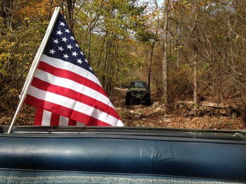 1979 Ford Bronco - An American flag is prominently displayed from a vehicle, with another Jeep navigating a trail in the woods.