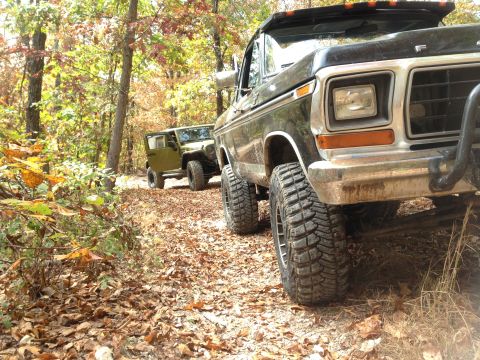 1979 Ford Bronco - Two off-road vehicles drive down a wooded path in the fall.