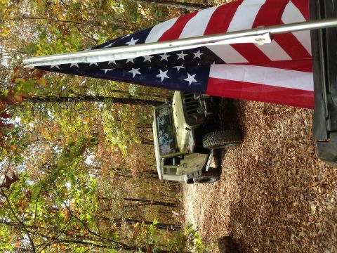1979 Ford Bronco - A Jeep Wrangler is parked on a wooded path during autumn, with an American flag draped above it.