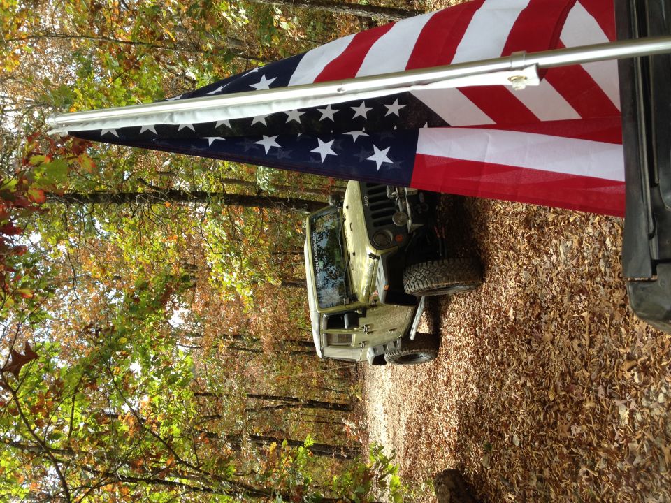 Jeep Wrangler parked on a leaf-covered path with an American flag overhead