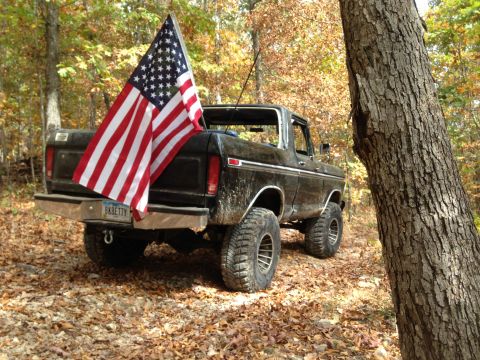 1979 Ford Bronco - A black 1979 Ford Bronco is parked off-road with an American flag attached to the rear.
