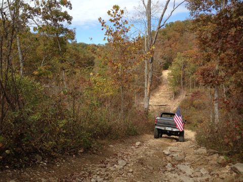 1979 Ford Bronco - Off-road vehicle with American flag ascends a steep, rocky path through autumn foliage.