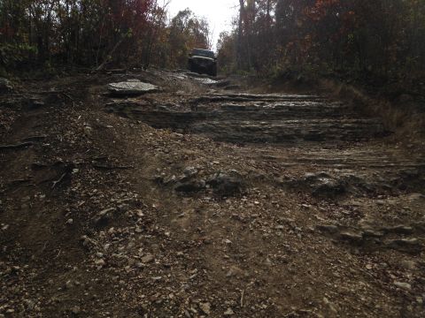 1979 Ford Bronco - A dark-colored SUV navigates a challenging, rocky off-road path during autumn.