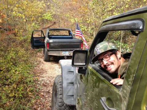1979 Ford Bronco - Two off-road vehicles drive down a dirt path in a wooded area during autumn.
