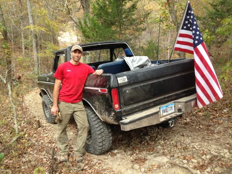 1979 Ford Bronco - A man poses with a black 1979 Ford F-150 pickup truck flying an American flag from the tailgate.