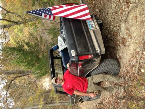 1979 Ford Bronco - A man poses with a black Ford Bronco flying an American flag, parked on a dirt trail during autumn.