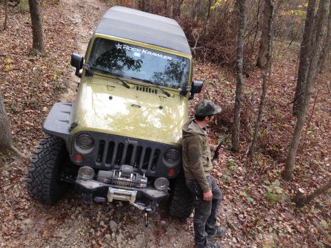 1979 Ford Bronco - Jeep Wrangler parked on a wooded trail during autumn. A person stands next to the vehicle.