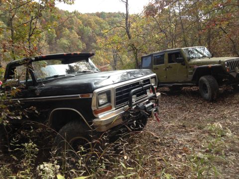 1979 Ford Bronco - Two off-road vehicles are parked on a dirt path surrounded by trees with autumn foliage.