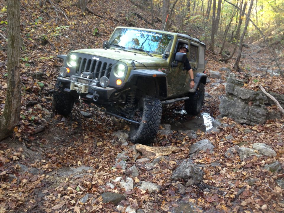 Green Jeep Wrangler off-roading on a rocky, leaf-covered trail.