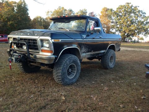 1979 Ford Bronco - A black 1979 Ford Bronco with large off-road tires and a winch mounted on the front bumper is parked on a grassy field. The vehicle has an…