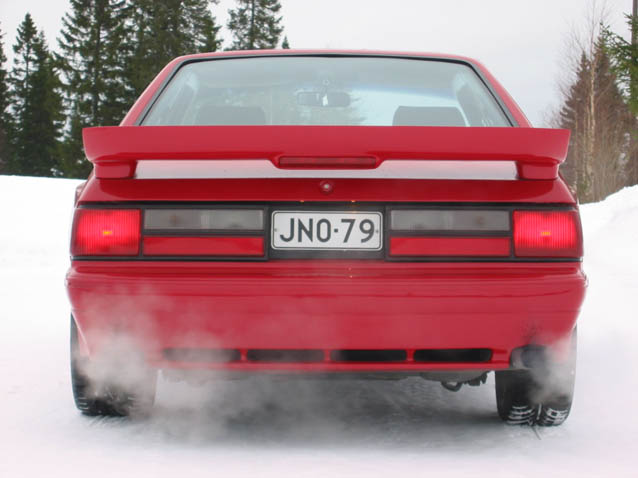 Rear of red hatchback coupe on snow with 'JNO-79' plate and exhaust vapor