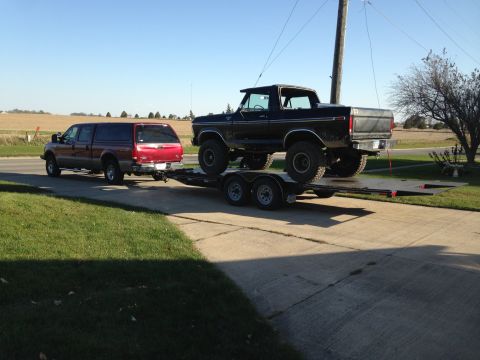 1979 Ford Bronco - A black 1979 Ford Bronco is loaded onto a flatbed trailer, which is being towed by a red Ford F-250 Super Duty pickup truck. The vehicles a…