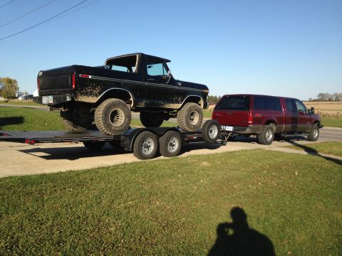 1979 Ford Bronco - A black Ford Bronco is loaded onto a trailer, being towed by a red Ford Excursion. The Bronco appears to be a lifted model with large tires…