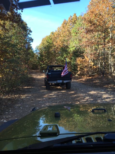 1979 Ford Bronco - A black Ford pickup truck with an American flag mounted on the tailgate drives down a dirt road lined with autumn trees. The photo is taken…